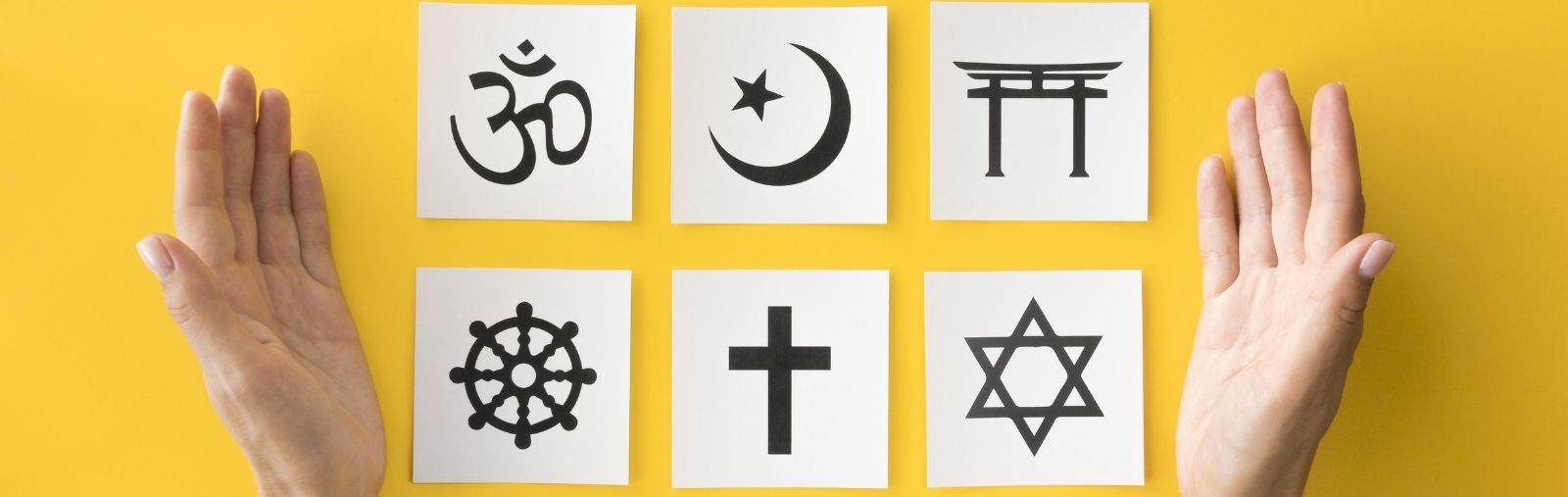 White pieces of paper with interfaith symbols on a yellow background, between two open hands