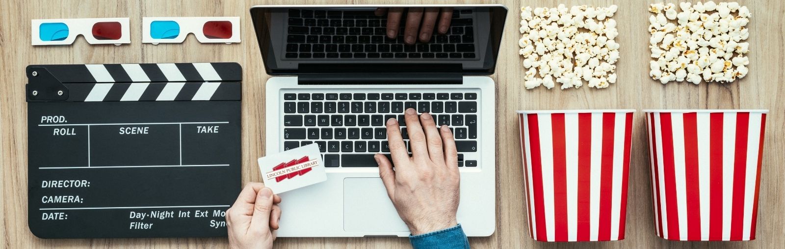 A man holding a library card typing on a laptop surrounding with popcorn and movie props