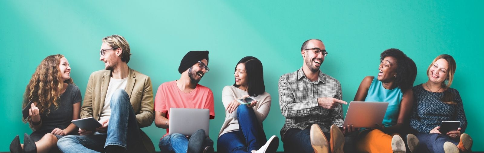 Pairs of people talk and laugh in front of a teal wall