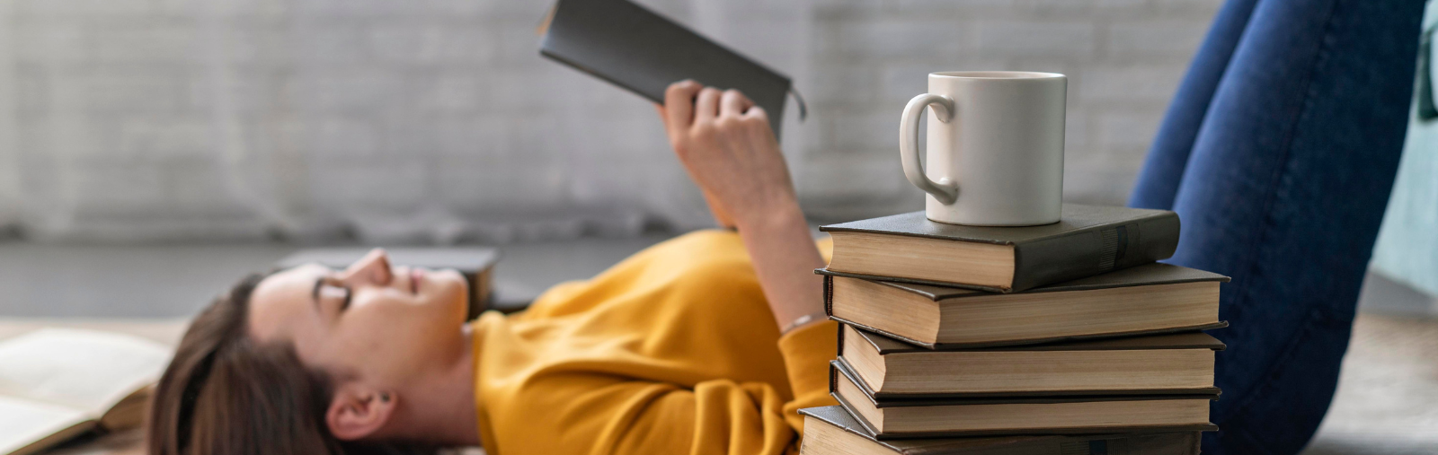 A teenage girl on her back reading behind a stack of books