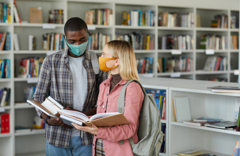 A man and woman wearing face coverings and looking at books