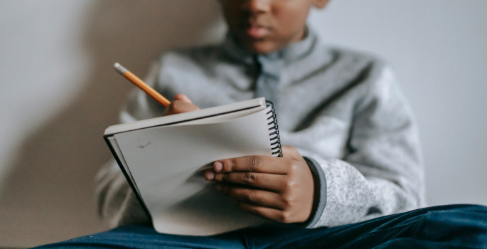 A young black boy writing in a notebook