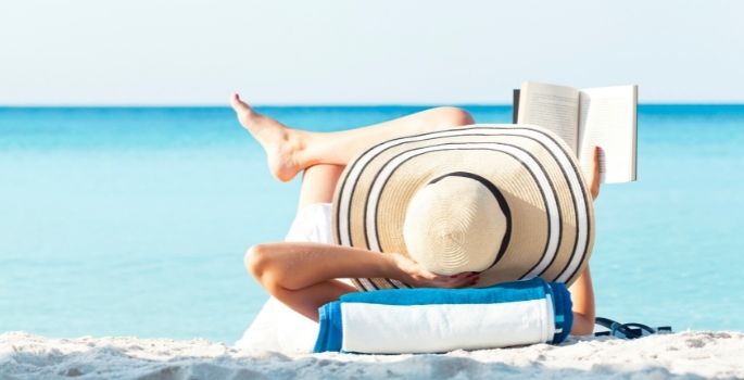 A woman in a sun hat reading on a beach