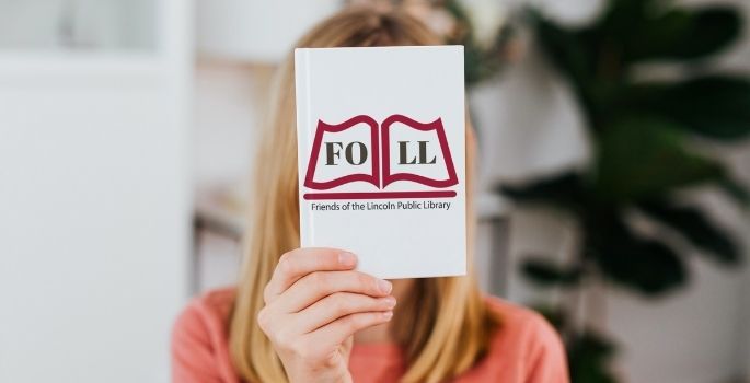 A woman holds a book with the Friends of the Lincoln Public Library logo in front of her face