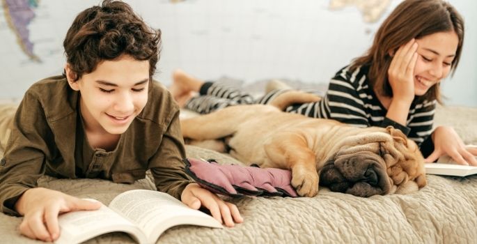 Two children on a bed reading to a dog