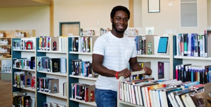 An African-American man pushes a cart of books in a library