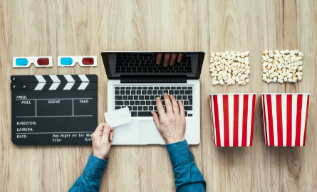 A table with clapperboard, laptop with someone typing, and two popcorn containers.