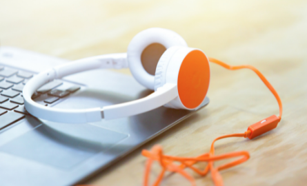 A pair of orange and white headphones plugged into a laptop