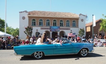 A blue car driving past the historic Civic Center in a parade