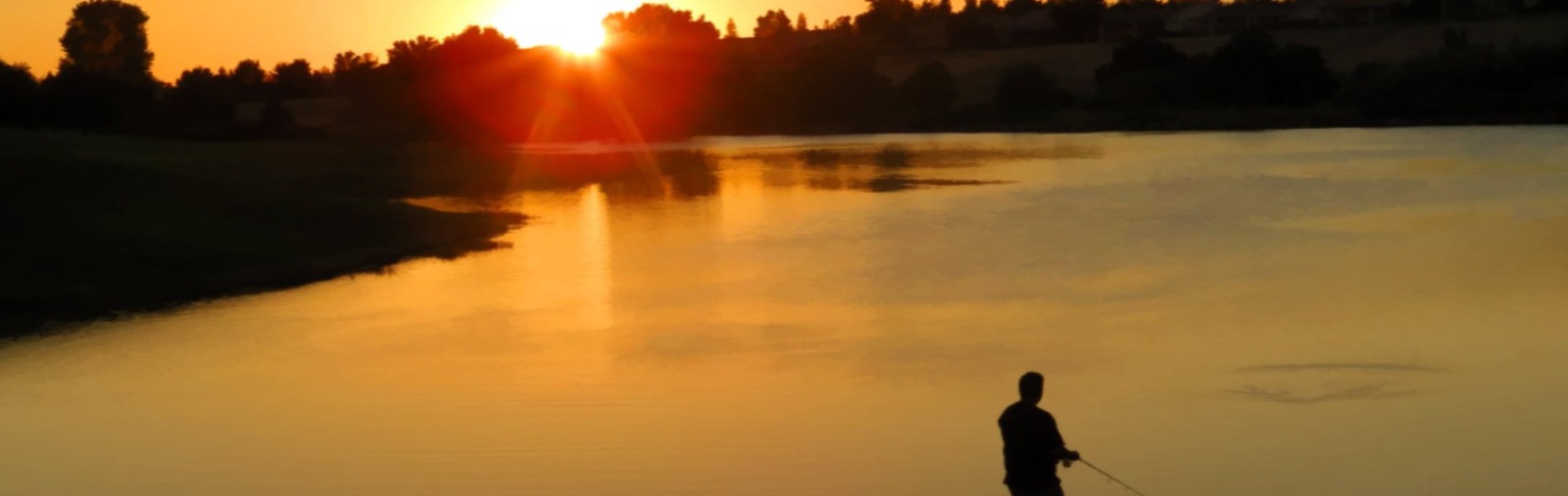 Man fishing at pond at sunset