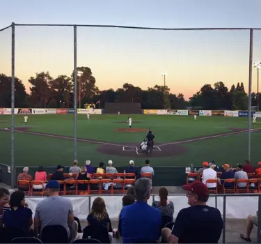 "People sitting with baseball game and sunset"